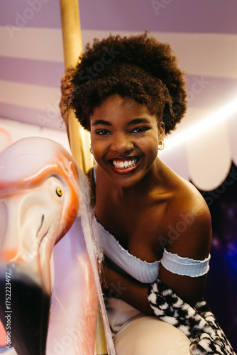 Portrait of a smiling young Black woman on a pink flamingo ride indoors