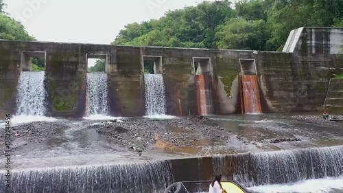Small Dam with Water Flowing Over and Lush Greenery in a Serene Natural Landscape.