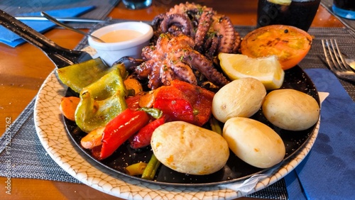 Traditional Canarian dish with grilled octopus, wrinkled potatoes, roasted bell peppers, green and red paprika, lemon slices, mojo sauce. Authentic Canary Islands cuisine served in local restaurant.