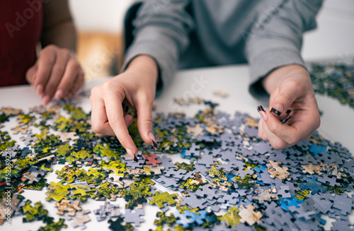 Girls Assembling Puzzle On A Table And Choosing Right Piece