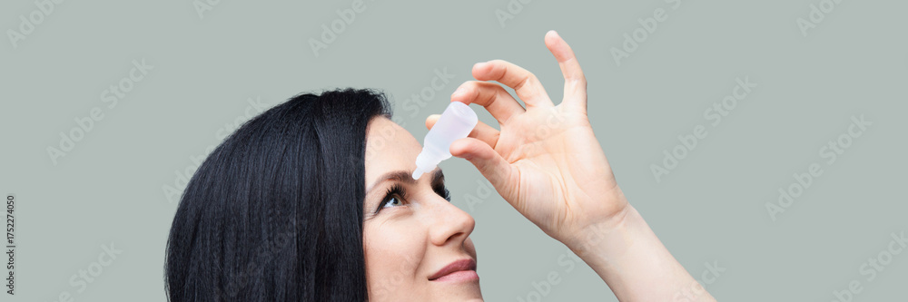 Fototapeta premium Caucasian female adult using eye drops against plain background for eye care and dryness relief.