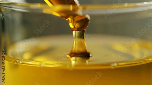 Macro slow-motion of golden cosmetic or cooking oil being dripped from a pipette into a glass beaker creating a viscous stream.
