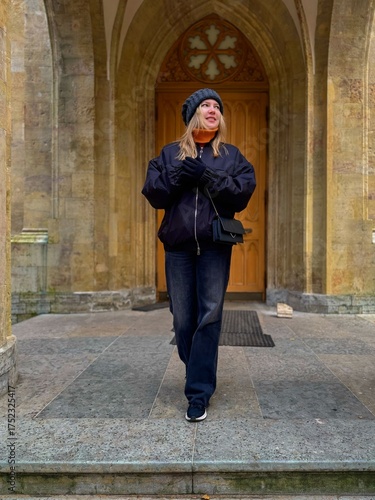 Stylish woman walks from historic stone archway with gothic wooden door