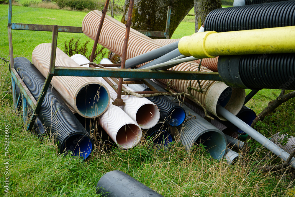 Fototapeta premium Stack of corrugated plastic drainage pipes and other construction materials resting on a rusty metal frame in long grass in Crich Derbyshire England