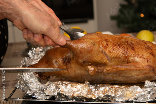 Chef skillfully cutting a beautifully roasted goose on aluminum foil, preparing a festive holiday meal during the joyful Christmas season