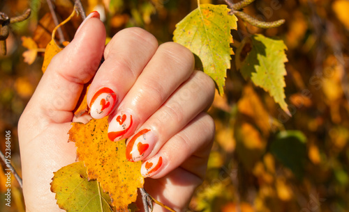 female hands with orange beautiful manicure on the background of autumn leaves