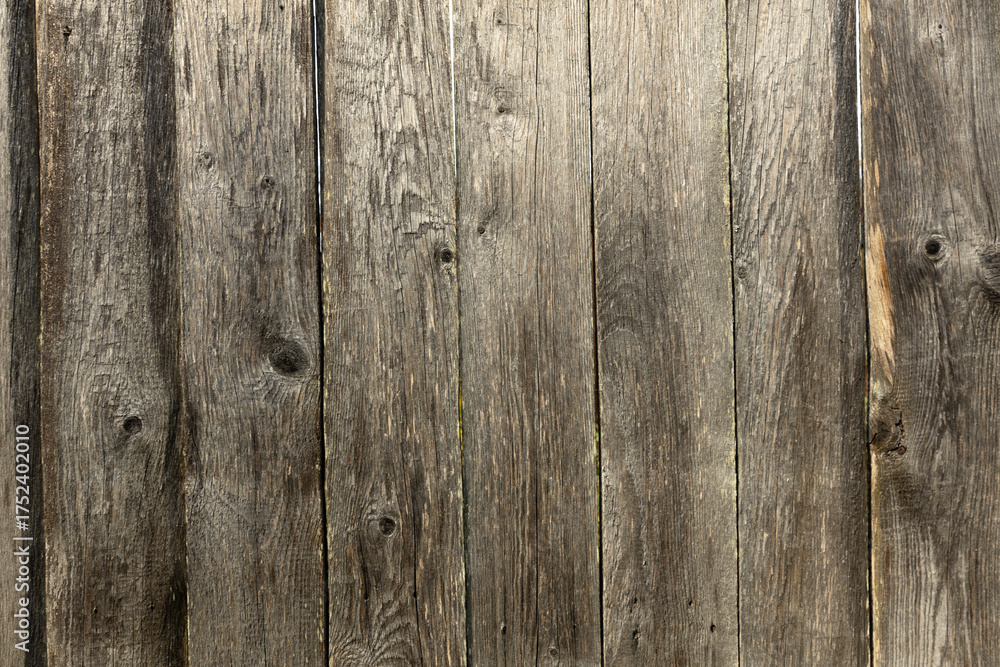 Fototapeta premium A close-up view of weathered wooden planks with a rustic texture. The wood shows signs of aging, with knots and varying shades of brown and gray.