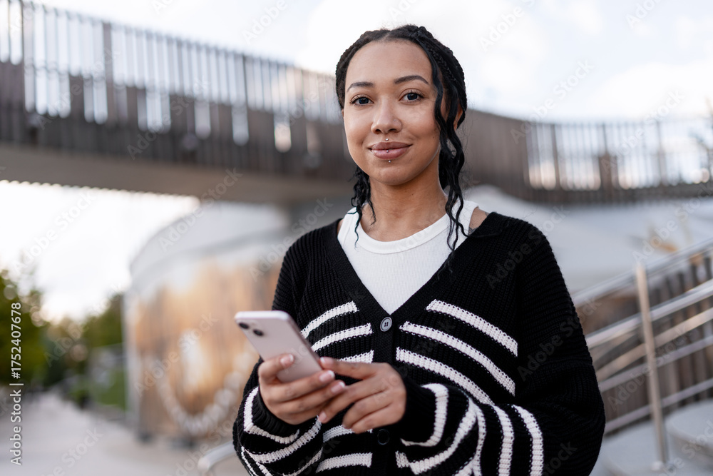 Fototapeta premium Young African American woman holding smartphone looking at camera using mobile app