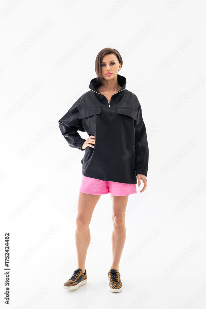 Fototapeta premium Elegant woman in black windbreaker jacket and pink shorts on light background. Fashionable female style. Studio photography. Vertical photo. High quality photo