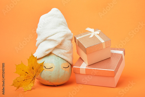 A pumpkin smeared with clay with a towel on top and gift boxes on an orange background, the time for holiday gifts and sales concept