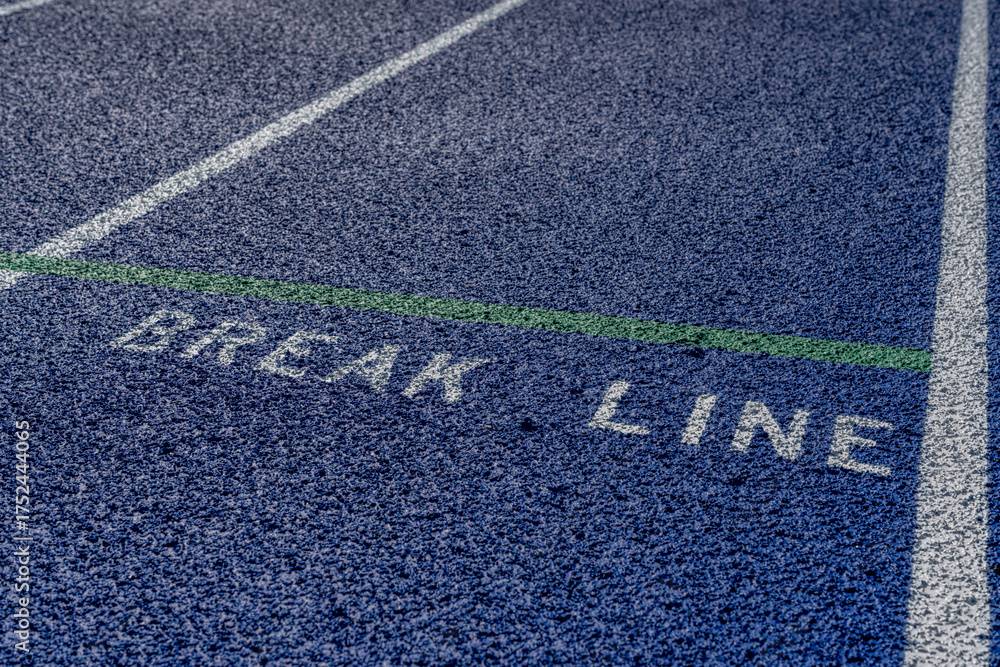Obraz premium Close up photo of outdoor blue running track with white lane lines, with the word, break line, on a new track.