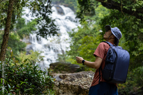 Asian hiker is trekking in the tropical forest with big waterfall for surveying and discovering the rare biological diversity and ecologist on the field study concept
