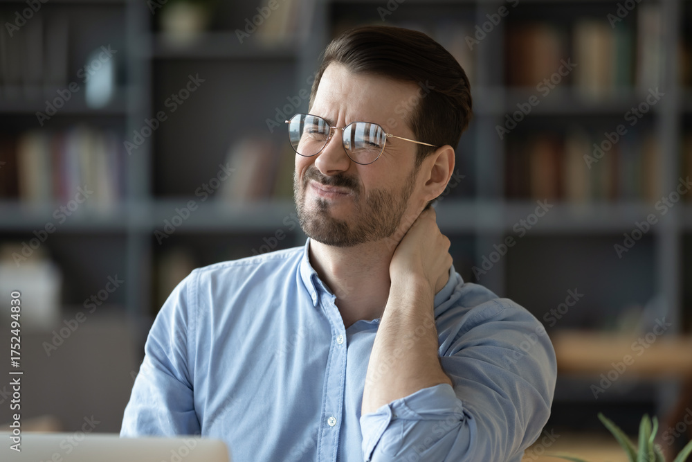 Fototapeta premium Tired young man grimacing with pain suffering from sore neck