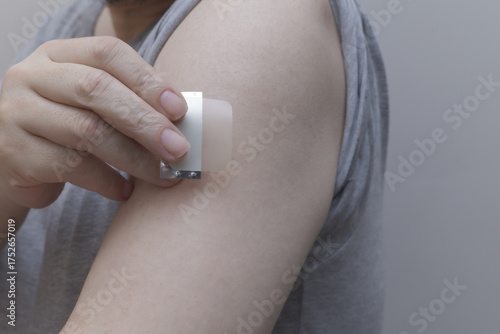 A close-up of a hand applying a nicotine patch to the upper arm. Represents Nicotine Replacement Therapy (NRT) and the user's commitment to quit smoking and pursue better health