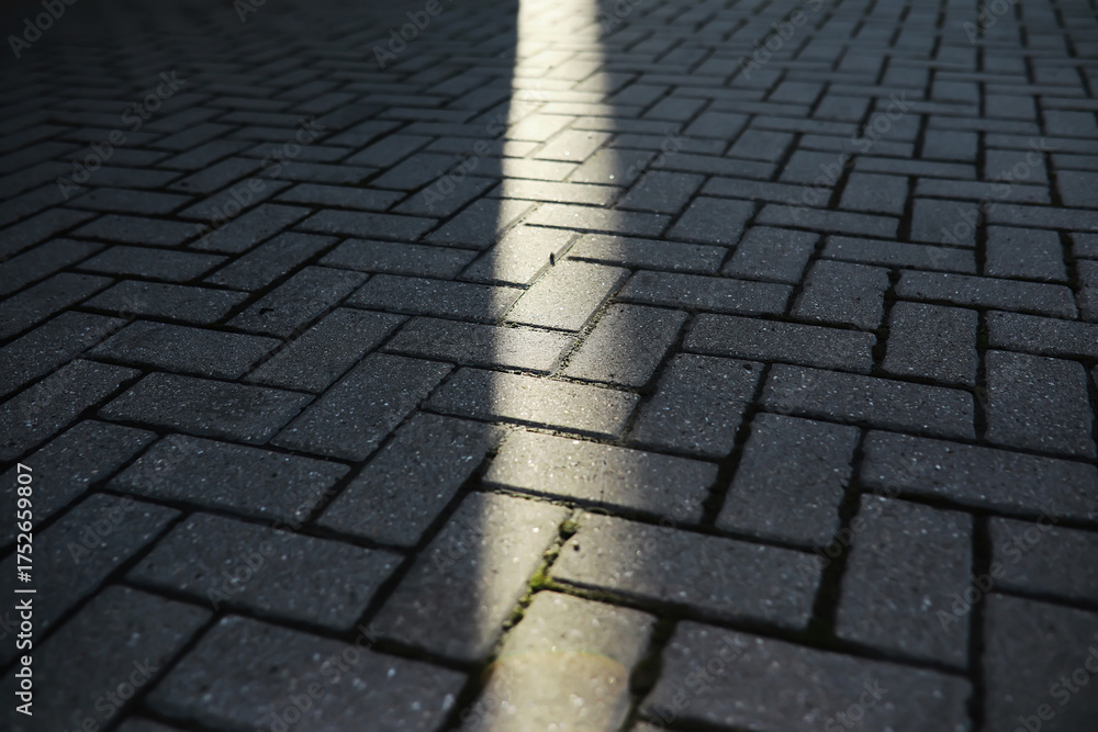 Fototapeta premium Sunlight Streaming Through a Narrow Gap on Patterned Brick Pavement