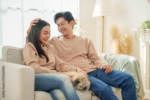 Happy Asian couple sitting close together on sofa, smiling and talking in a warm home atmosphere full of love and relaxation.