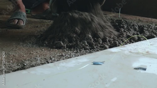 Professional construction workers prepare equipment and apply a thick layer of adhesive to the ceramic tiles to attach them to the walkway surface.