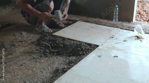 Professional construction workers prepare equipment and apply a thick layer of adhesive to the ceramic tiles to attach them to the walkway surface.