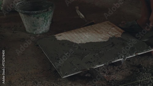 Professional construction workers prepare equipment and apply a thick layer of adhesive to the ceramic tiles to attach them to the walkway surface.