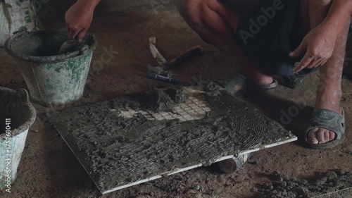 Professional construction workers prepare equipment and apply a thick layer of adhesive to the ceramic tiles to attach them to the walkway surface.