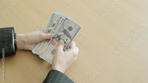Businessperson counting hundred-dollar bills on wooden desk, concept of finance, savings, and investment for success and wealth.