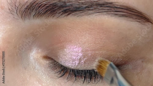 Applying pink eyeshadow to the eyelids. Close-up video of beautiful female face make up with cosmetic brush.
