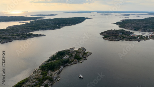 Drone Aerial of Island Channel Near Strömstad, Sweden with Rocky Shores, Greenery, and a White Boat Floating on Calm Water at Sunset