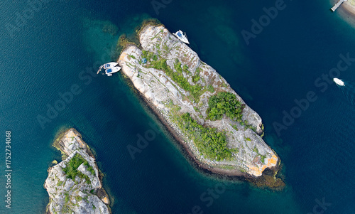 Top-Down Aerial View of Small Rocky Island Near Strömstad, Sweden with Green Vegetation and Boats Moored Along the Shore in Clear Blue Water
