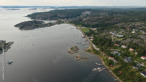 Aerial View of Coastal Town Near Strömstad, Sweden with Waterfront Houses, Rocky Hills, Docks, and Calm Sea Under Cloudy Skies
