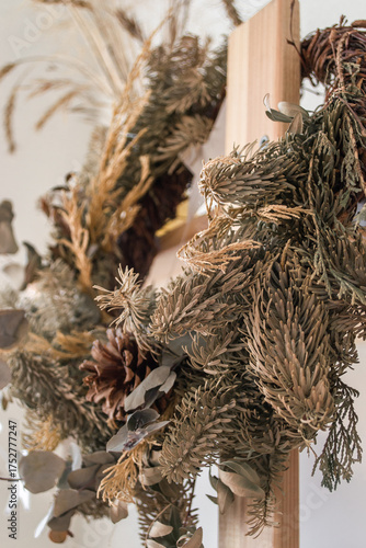 dried flower wreath adorned with various natural elements hangs on wooden frame against light wall. warm tones and textures create cozy atmosphere in room. vertical. close up.