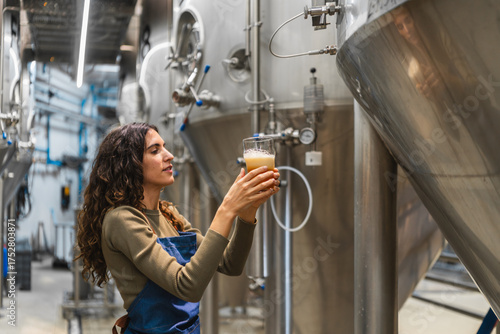 Photos Woman brewer evaluating beer sample, producing craft beer in a modern brewery wi