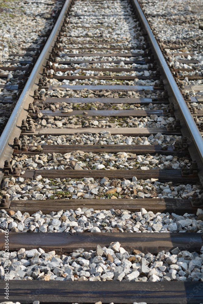 Naklejka premium A straight section of railroad tracks extends into the distance, featuring metal rails, wooden sleepers, and bright gravel ballast in a close-up perspective