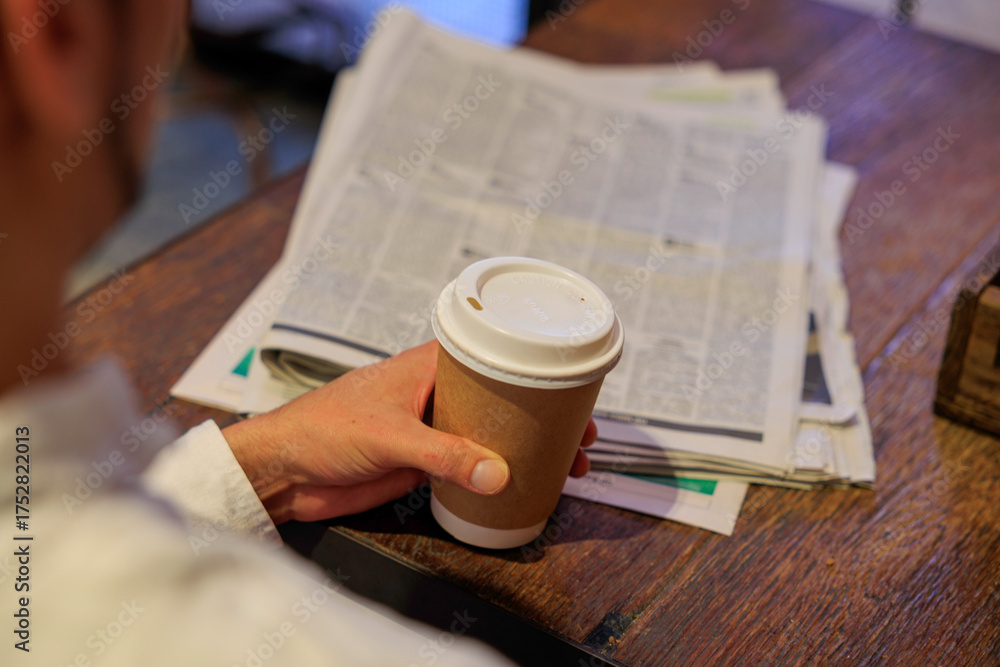 Naklejka premium テーブルの上で新聞を広げてコーヒーを飲む手元
