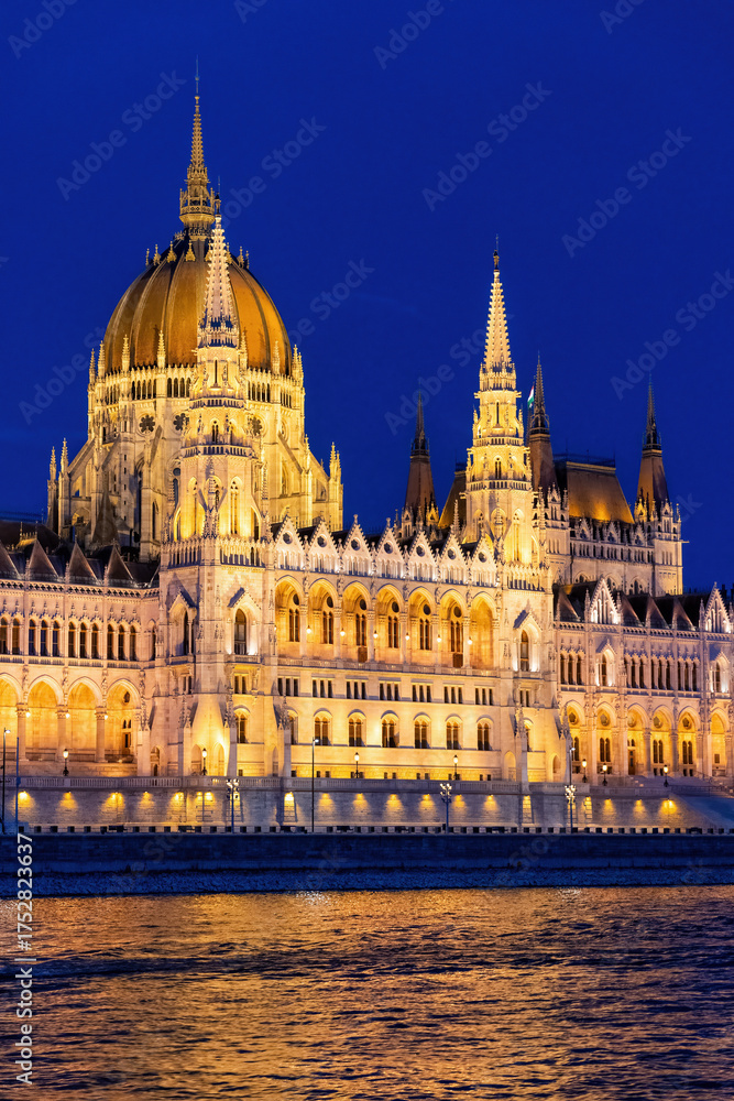 Fototapeta premium The Hungarian Parliament Building in Budapest glows under the night sky. Reflection shimmers in the waters of the Danube River