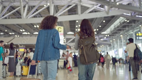 Latino woman walking through airport terminal to boarding gate with friend.
