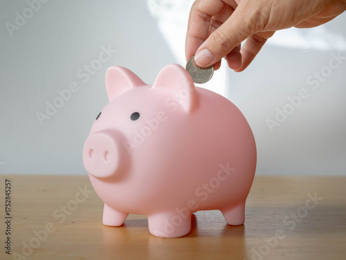 Close-up of a Hands a coin Pink piggy bank on a desk with a jar saving money