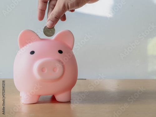 A Hands a coin Pink piggy bank on a desk with a jar saving money