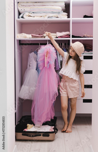 A little girl of European appearance puts things in a suitcase in a dressing room. Preparation, getting ready for a vacation trip