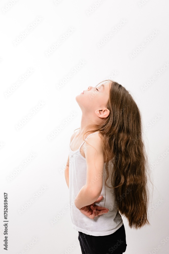 Obraz premium Young girl with long brown hair looking up, peaceful expression against a white background.