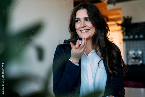 Businesswoman using smartphone for voice command at office smiling