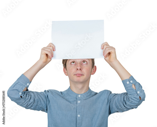 Confused teenage boy keeps a blank paper sheet over head looks up bewildered. Male adolescent portrait holding an empty banner placard, isolated on transparent background