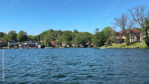 Peaceful lake view with reflections of waterfront houses and lush green trees. Calm water and clear sky create a relaxing summer landscape. Perfect for travel, nature, and lifestyle themes.