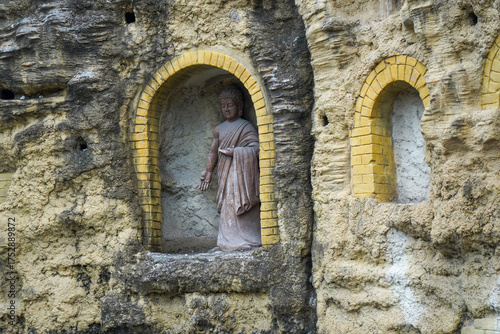 Buddha statue in arched niche carved in rocky wall