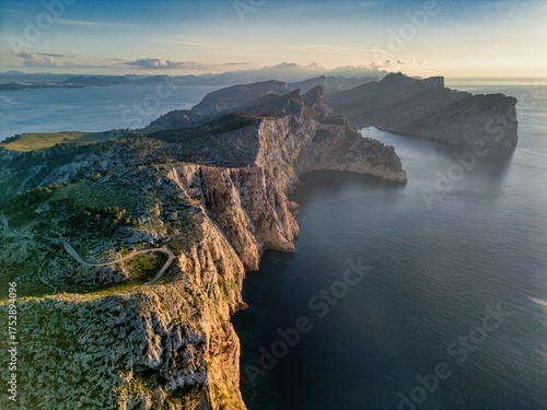 Aerial view of rugged cliffs meeting the deep blue sea, with the sun casting long shadows on the Cap de Formentor, Balearic Islands, Spain.