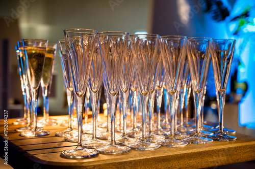 Row of champagne glasses filled with sparkling wine arranged on wooden table under warm light. Elegant setup for festive event or wedding celebration with luxurious atmosphere.
