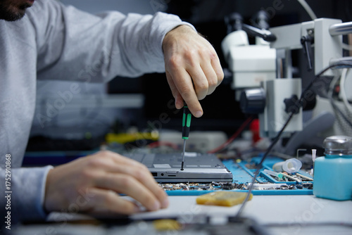 A technician is carefully repairing a circuit board with precision tools in a workshop