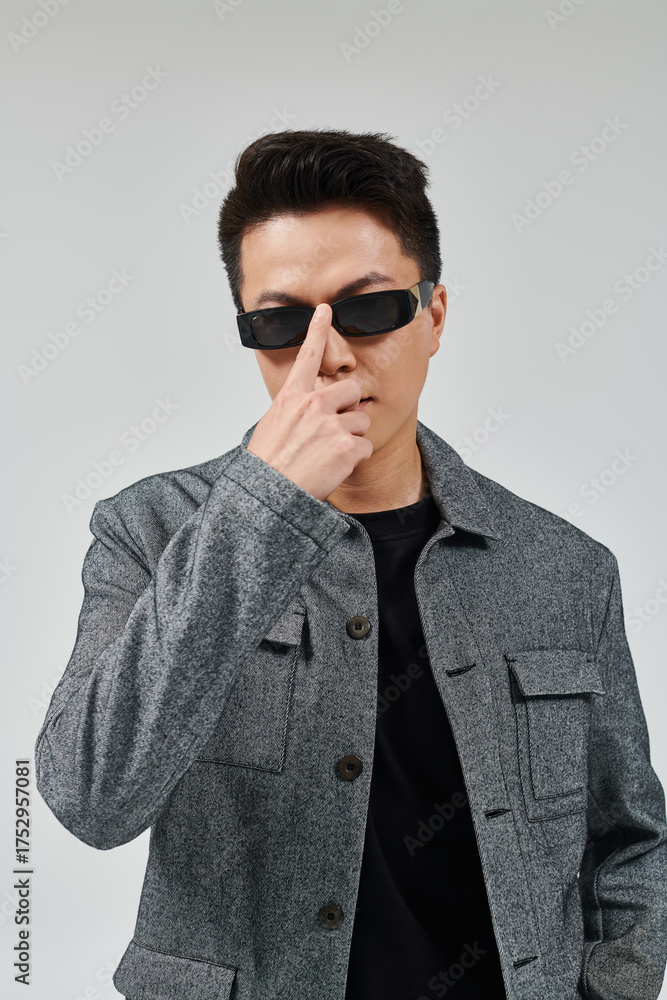 Obraz premium Confident young Asian man showing style while wearing sunglasses against a simple background