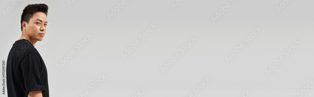 Fototapeta premium Handsome young Asian man standing confidently against a minimalist gray backdrop