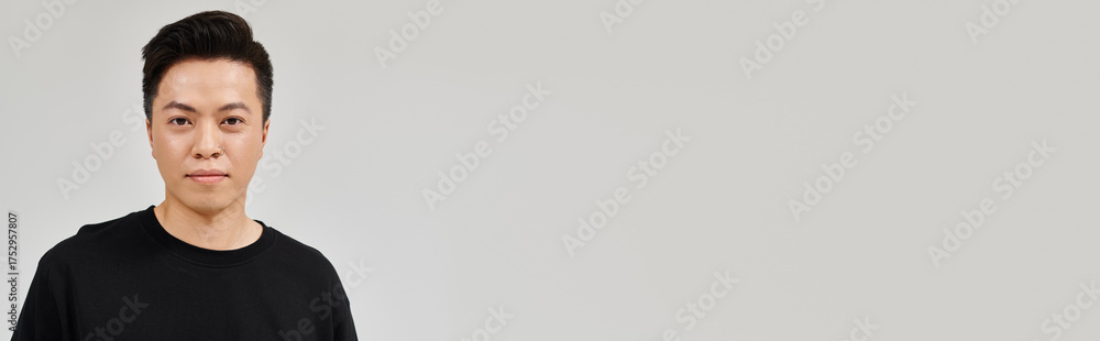 Fototapeta premium Young Asian man poses confidently in casual attire against a minimalist backdrop