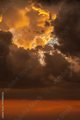 Golden sunset clouds glowing through stormy skies, capturing light, shadow and emotion in the evening. Fiery clouds clash with darkness as sunlight breaks through, painting the sky.